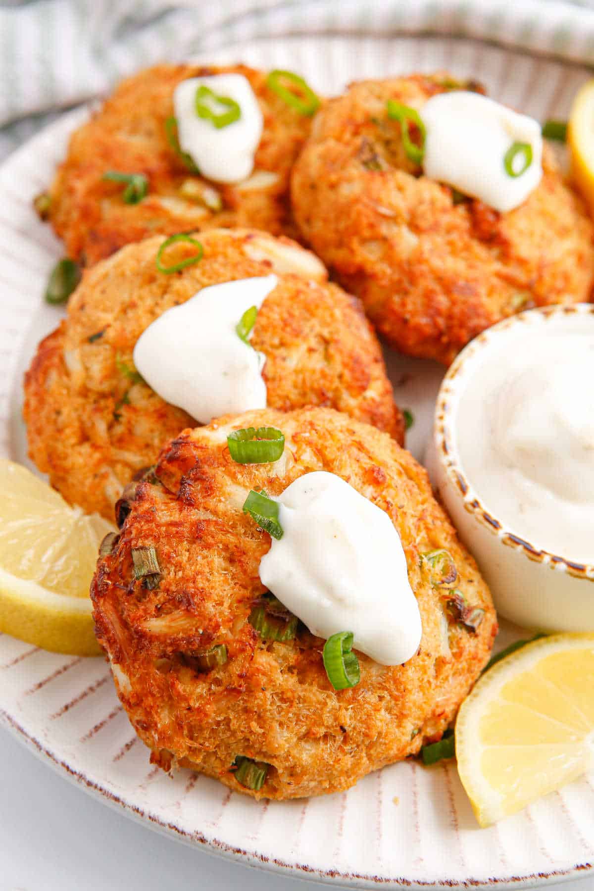 Air fryer crab cakes topped with tartar sauce and green onions.