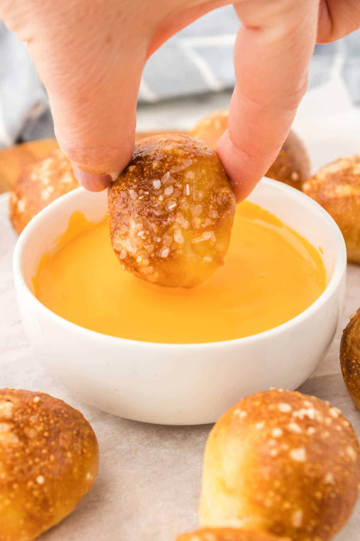 A hand dipping a pretzel bite into cheese sauce.