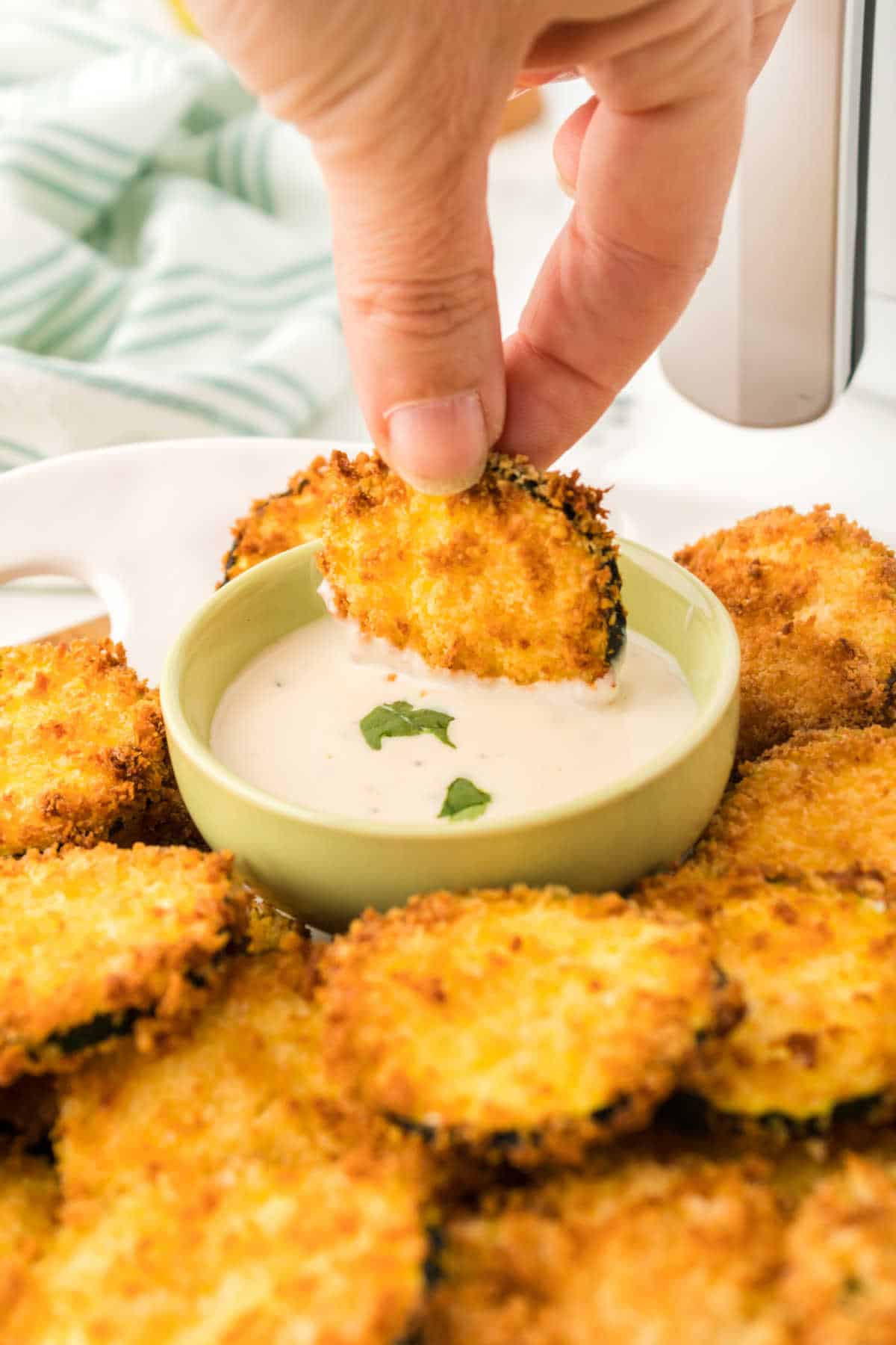 A hand dipping an air fryer zucchini chip in dipping sauce.