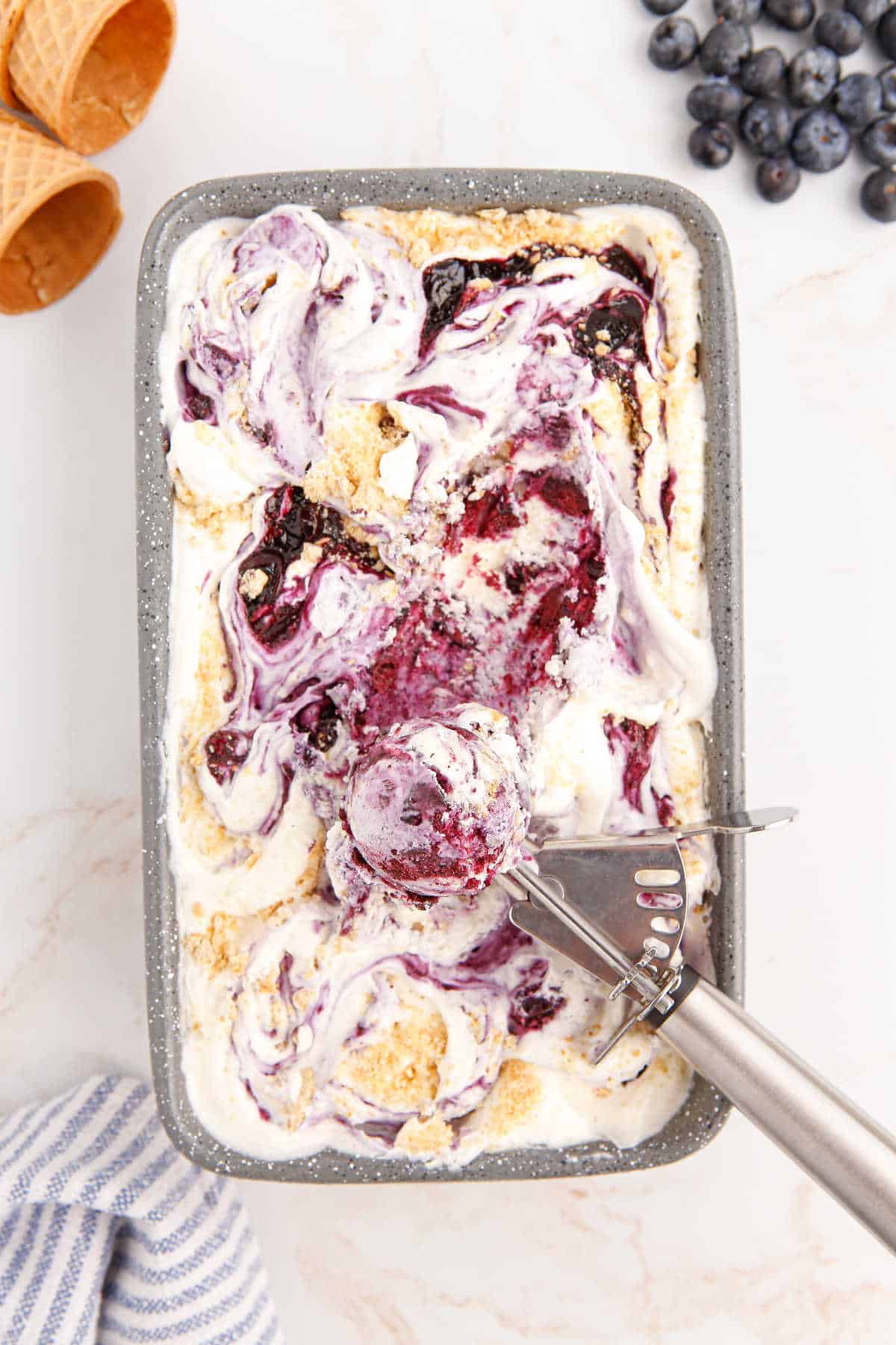 Blueberry pie ice cream in a loaf pan with an ice cream scoop.
