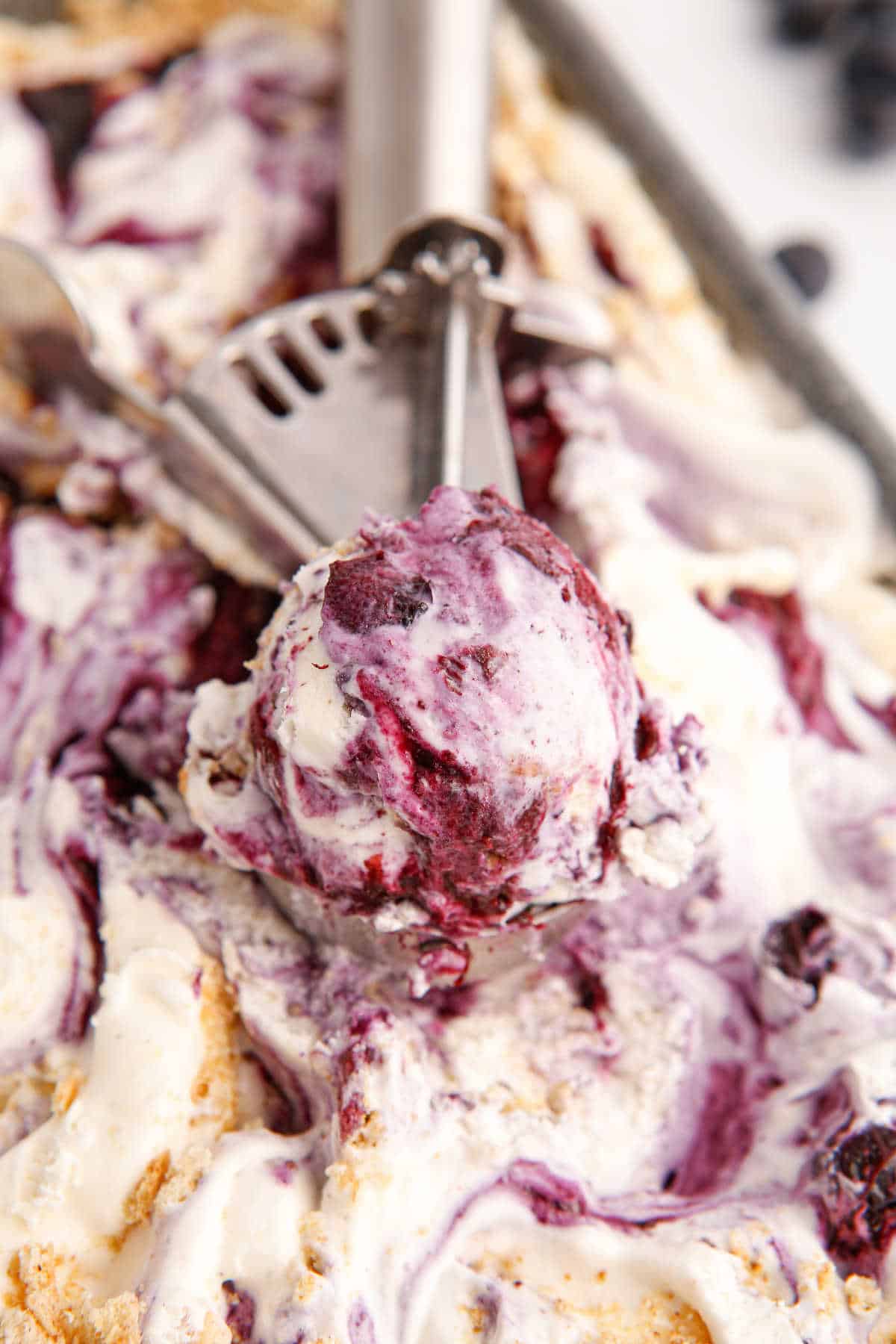 An ice cream scoop in a tub of blueberry pie ice cream.