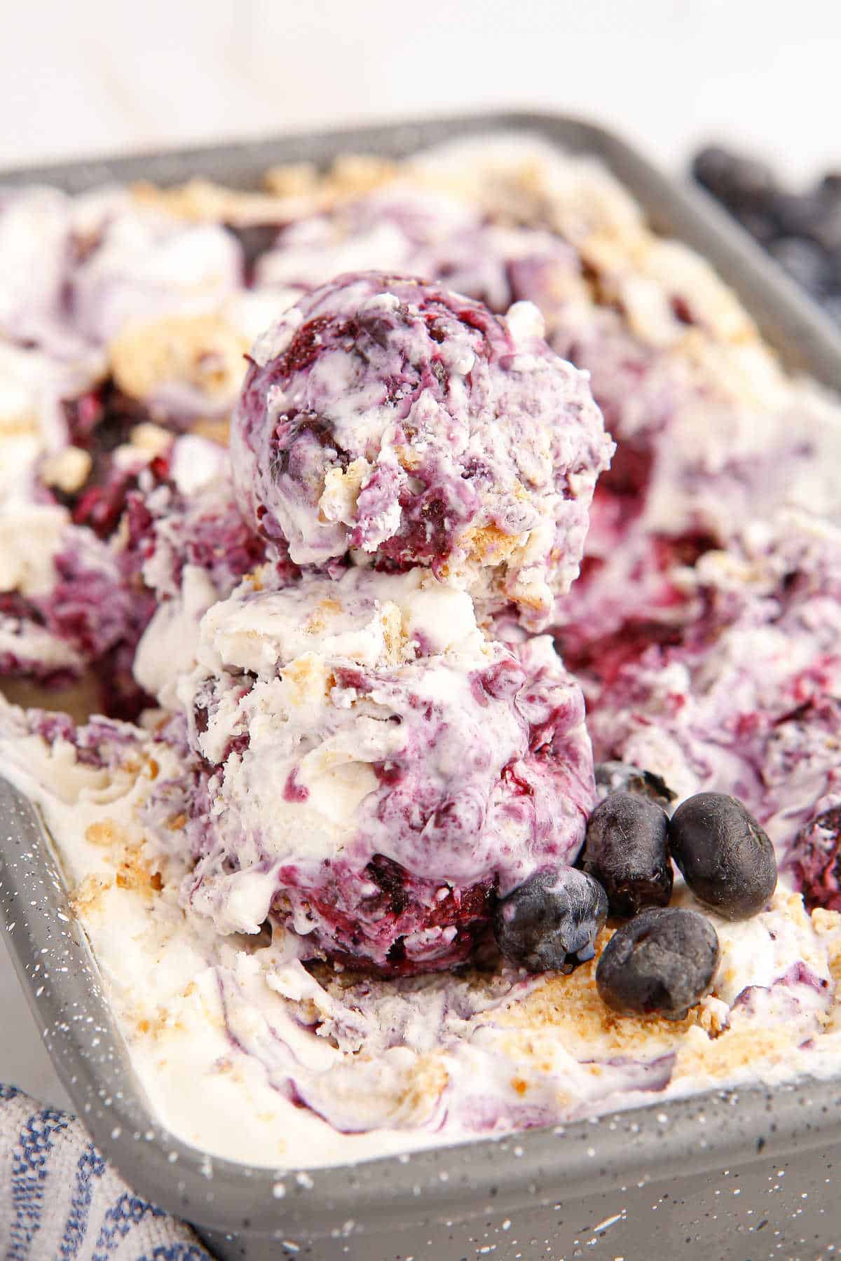 A loaf pan of blueberry pie ice cream with scoops on top and fresh blueberries.