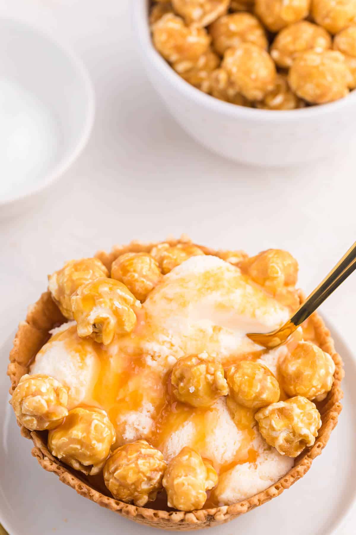 Caramel crunch ice cream sundae on a plate with a small gold spoon in it.