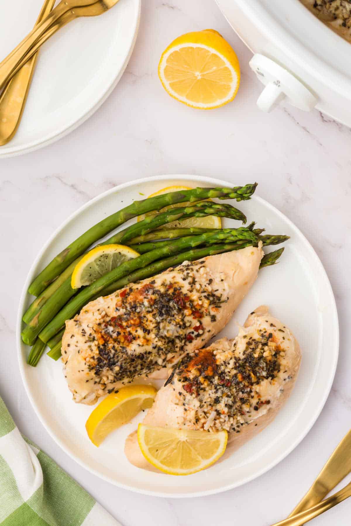 Crockpot Lemon Garlic Butter Chicken on a plate with asparagus and lemon slices.