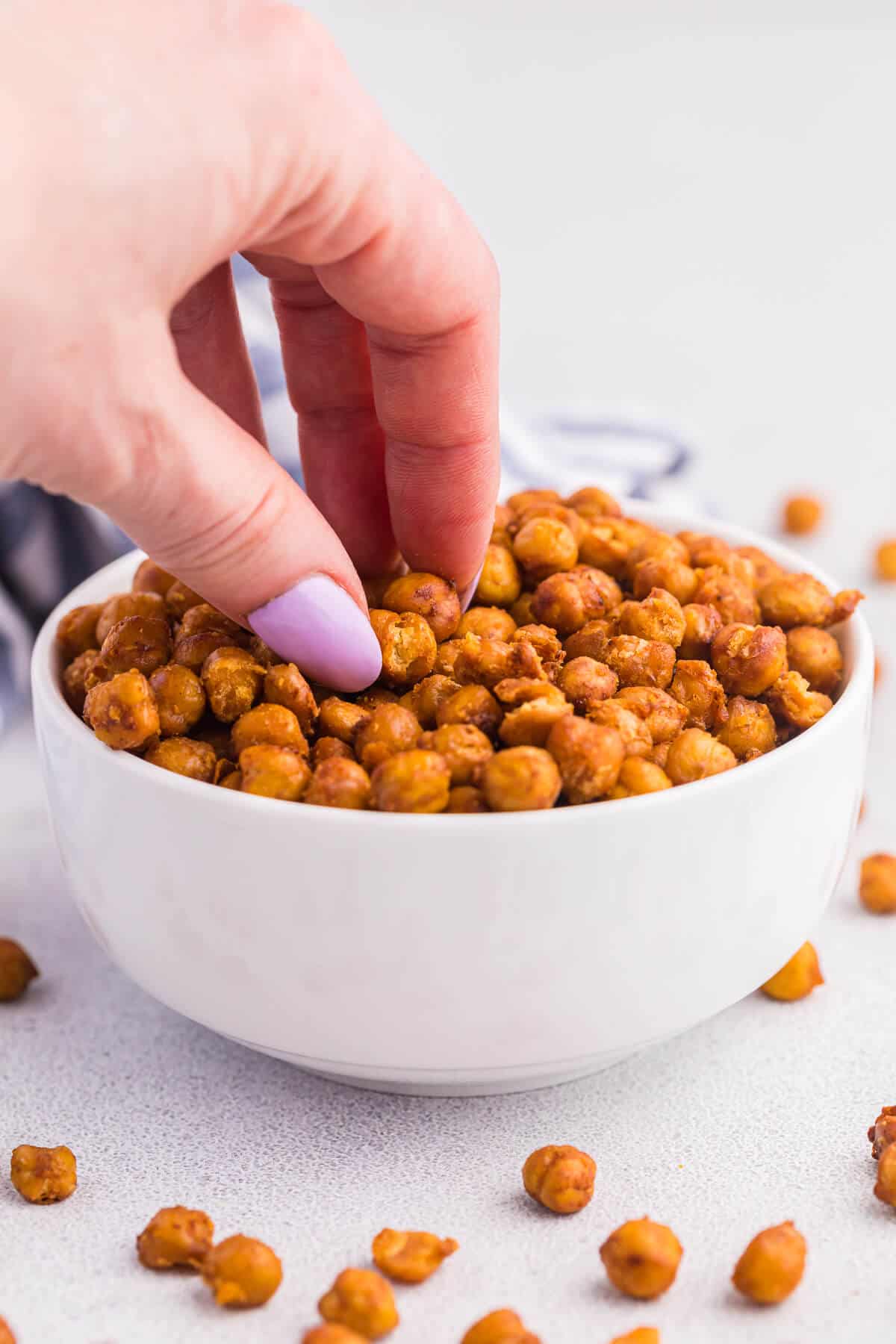 A hand reaching in a bowl of taco roasted chickpeas.