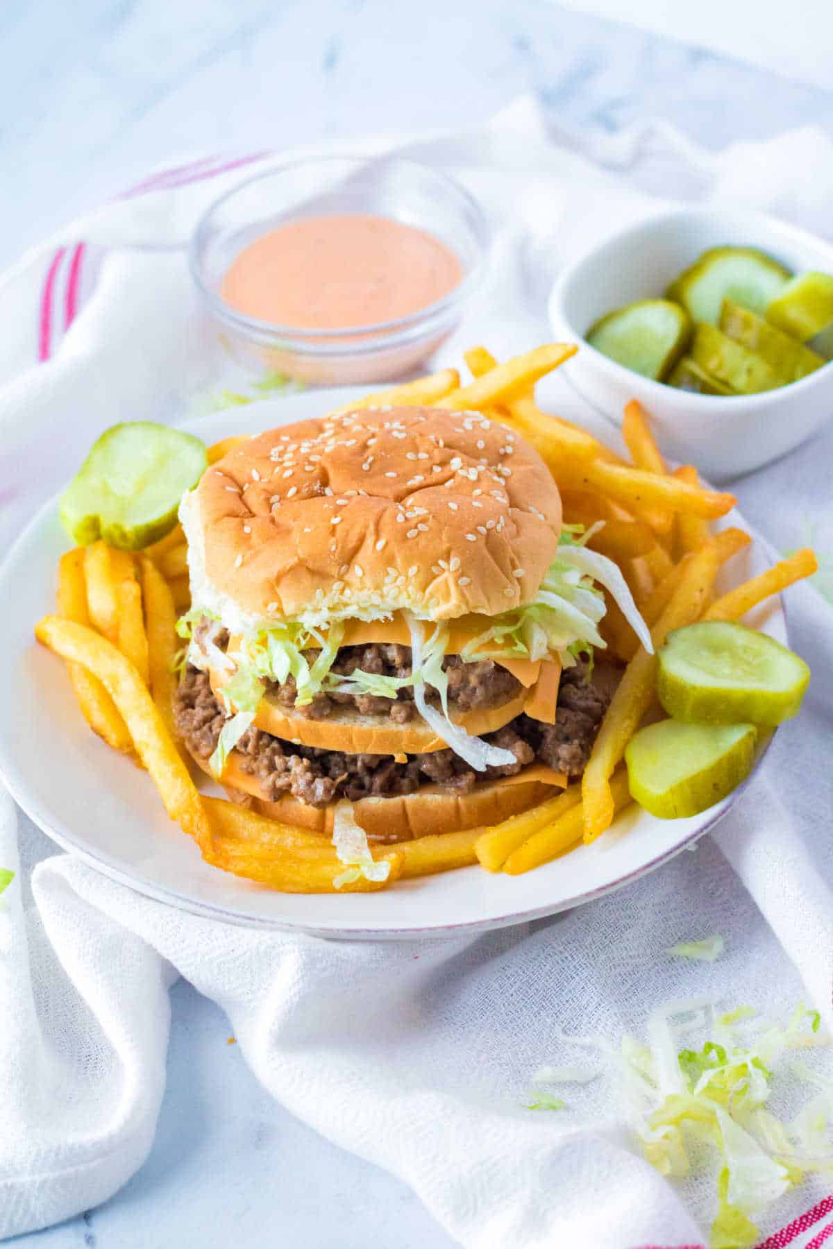 A big mac sloppy joe on a plate with fries and pickles.