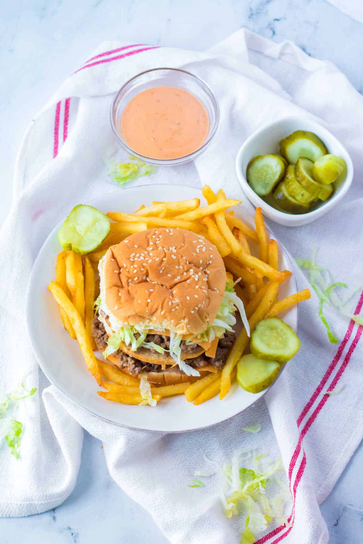A big mac sloppy joe on a plate with fries and pickle slices.