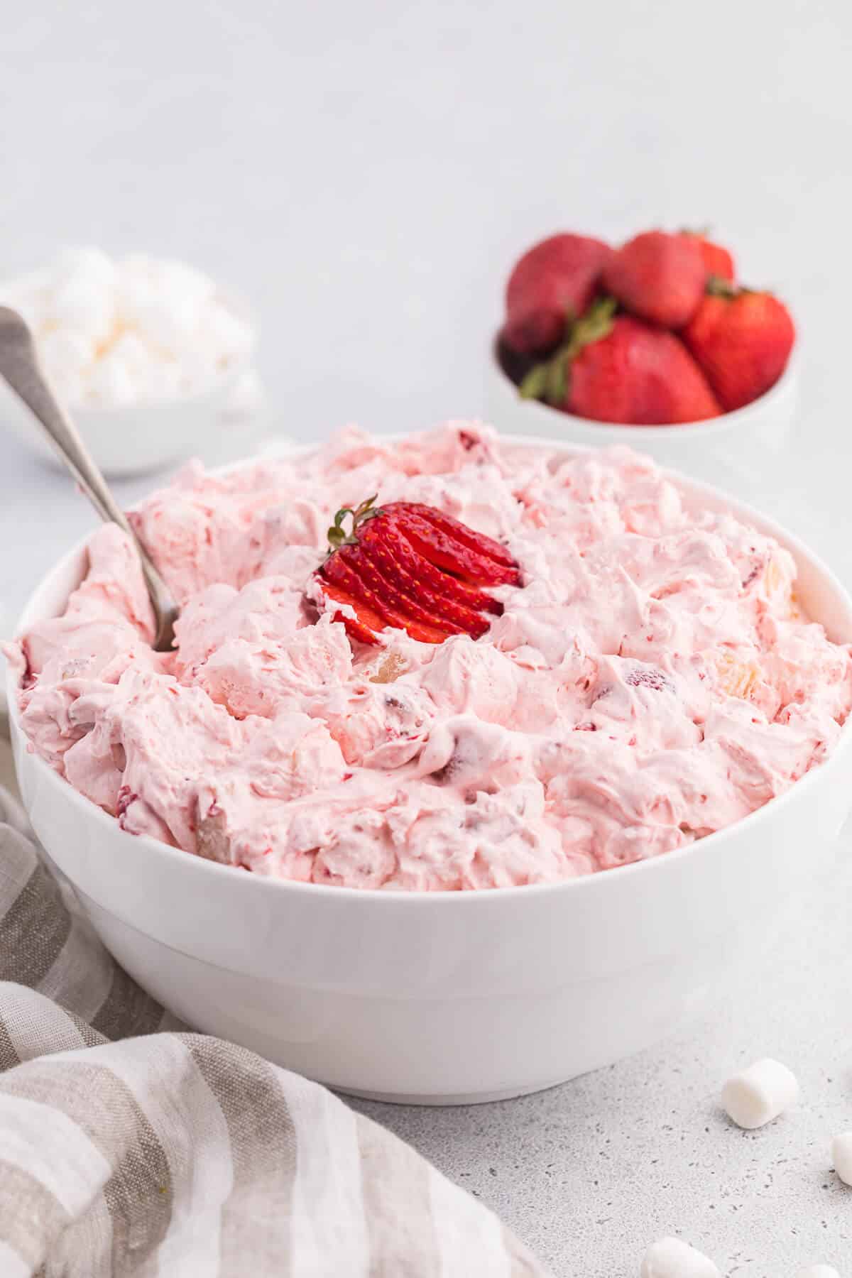 Strawberry fluff salad in a white bowl with a spoon.