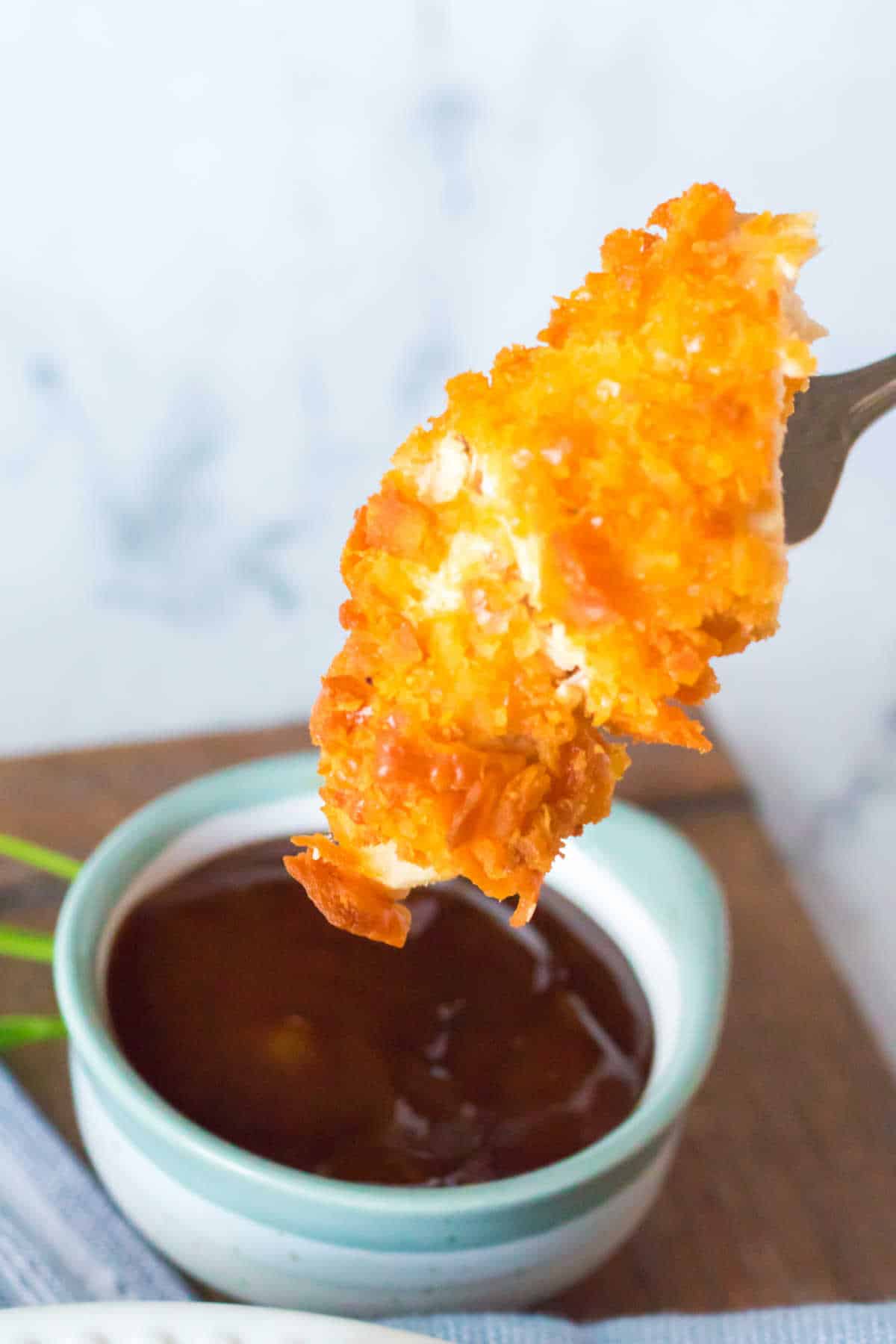 A fork dipping a chicken tender in BBQ sauce.