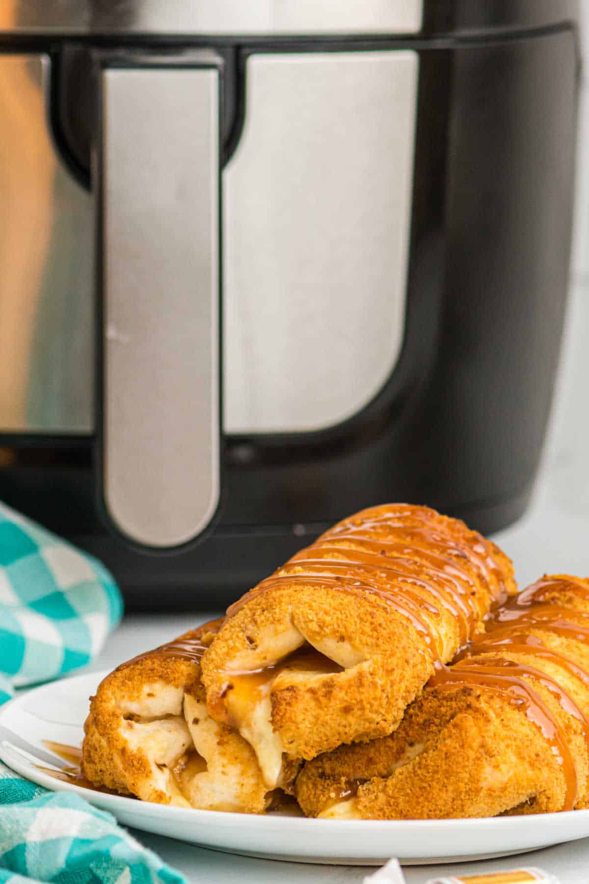 Air fryer caramel cheesecake chimichangas on a plate in front of an air fryer.