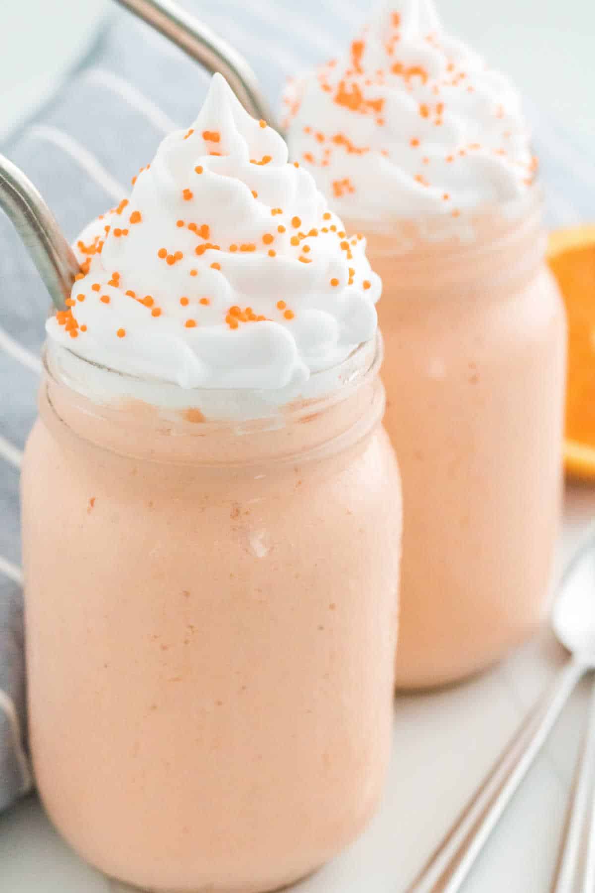 Two boozy orange creamsicle milkshakes with metal straws.