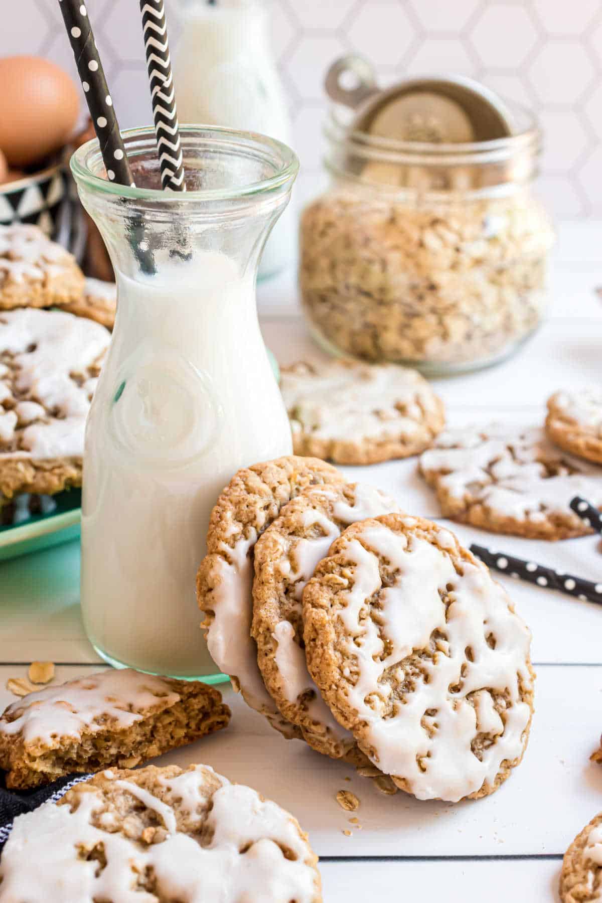 Three iced oatmeal cookies leaning up against a glass of milk.