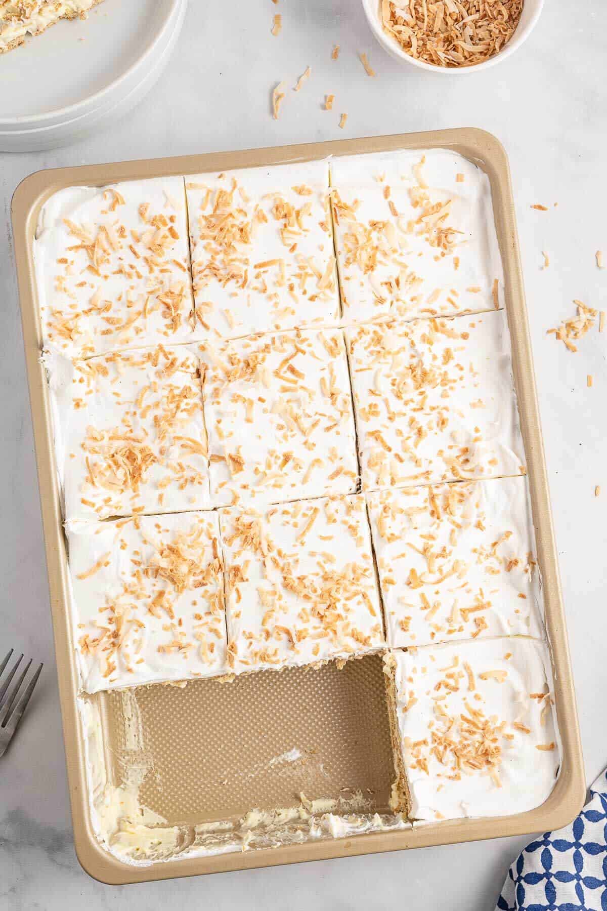 A pan of coconut icebox cake cut into squares with two pieces missing.