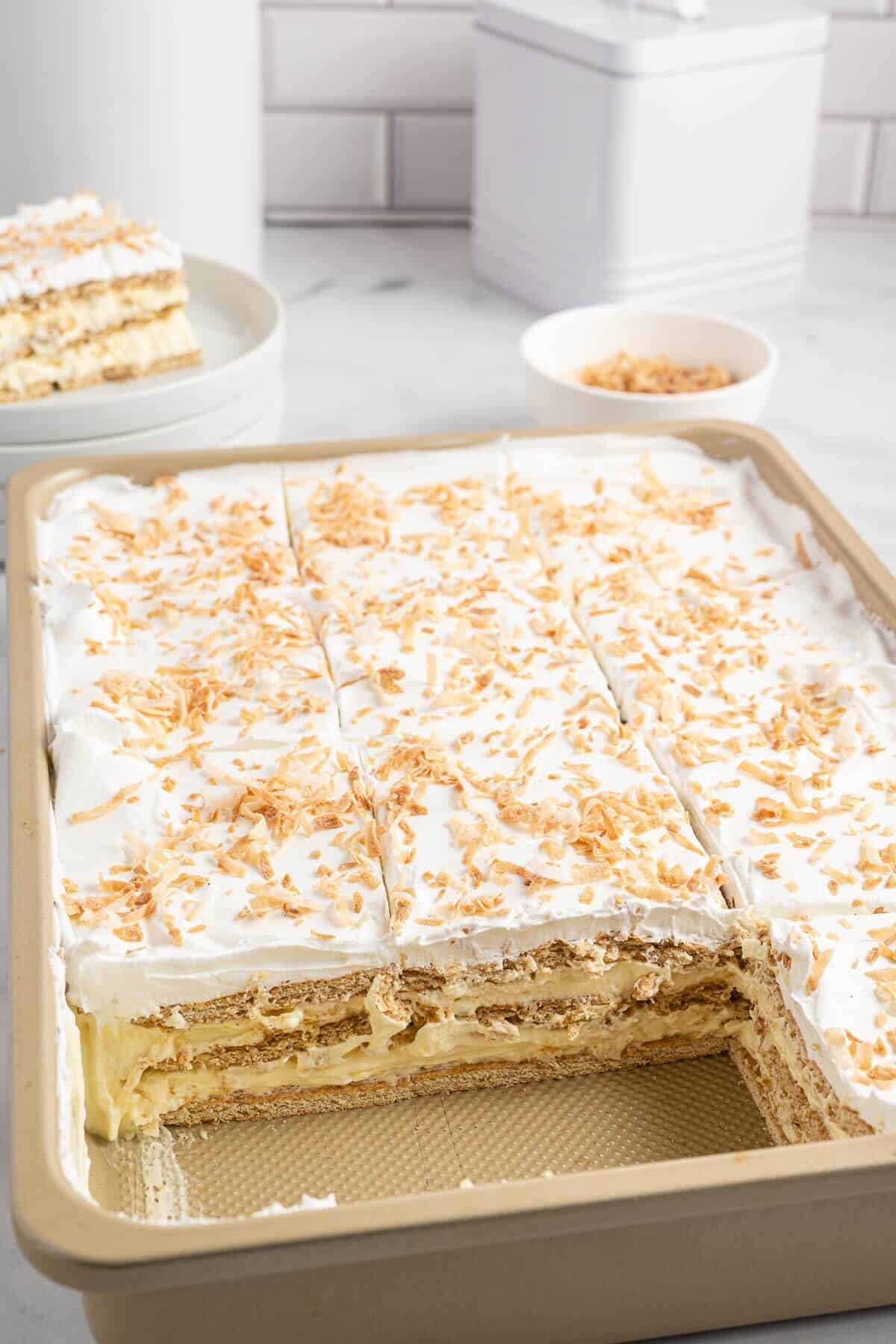 A pan of coconut icebox cake with pieces missing out of it.