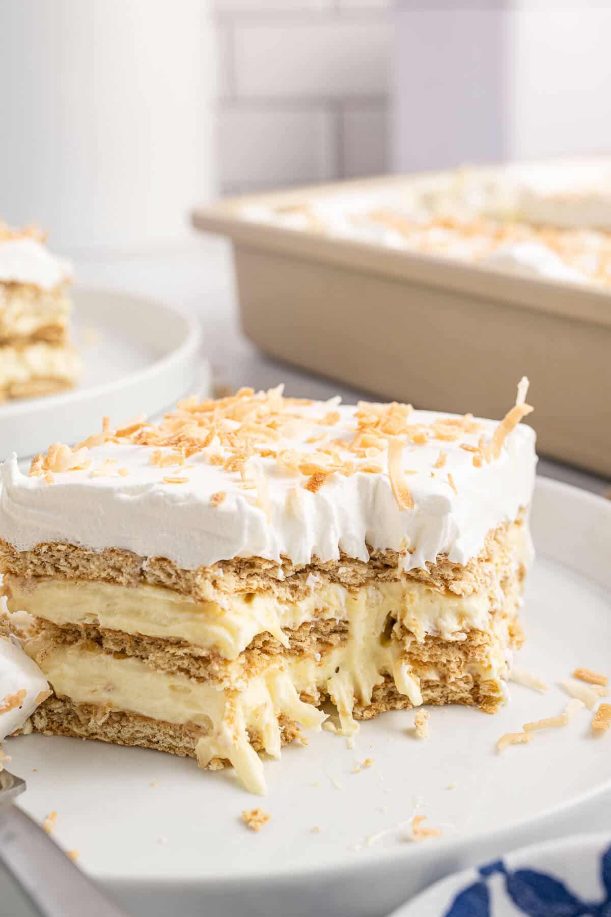 A piece of coconut icebox cake on a plate with a bite taken out of it.