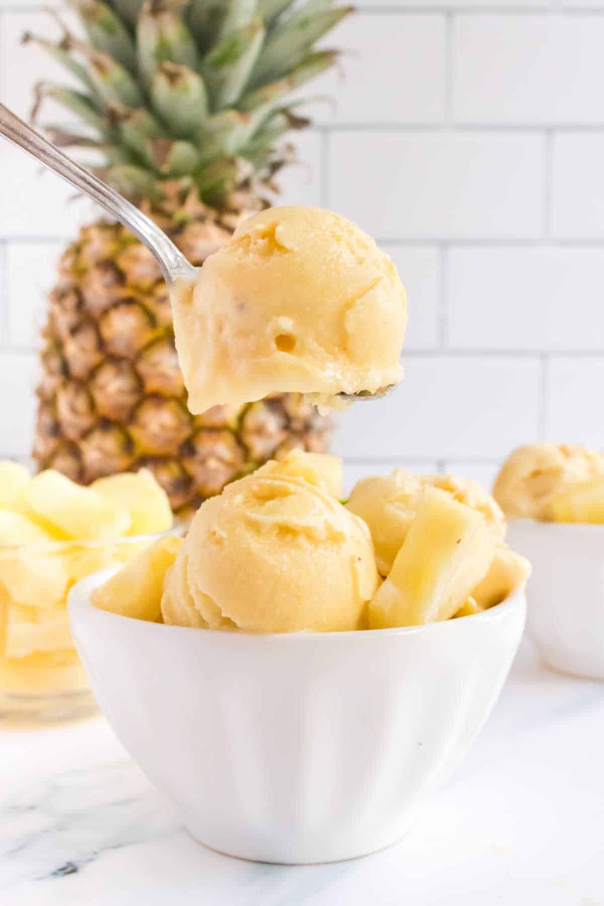 Pineapple ice cream on a spoon over a bowl of ice cream.