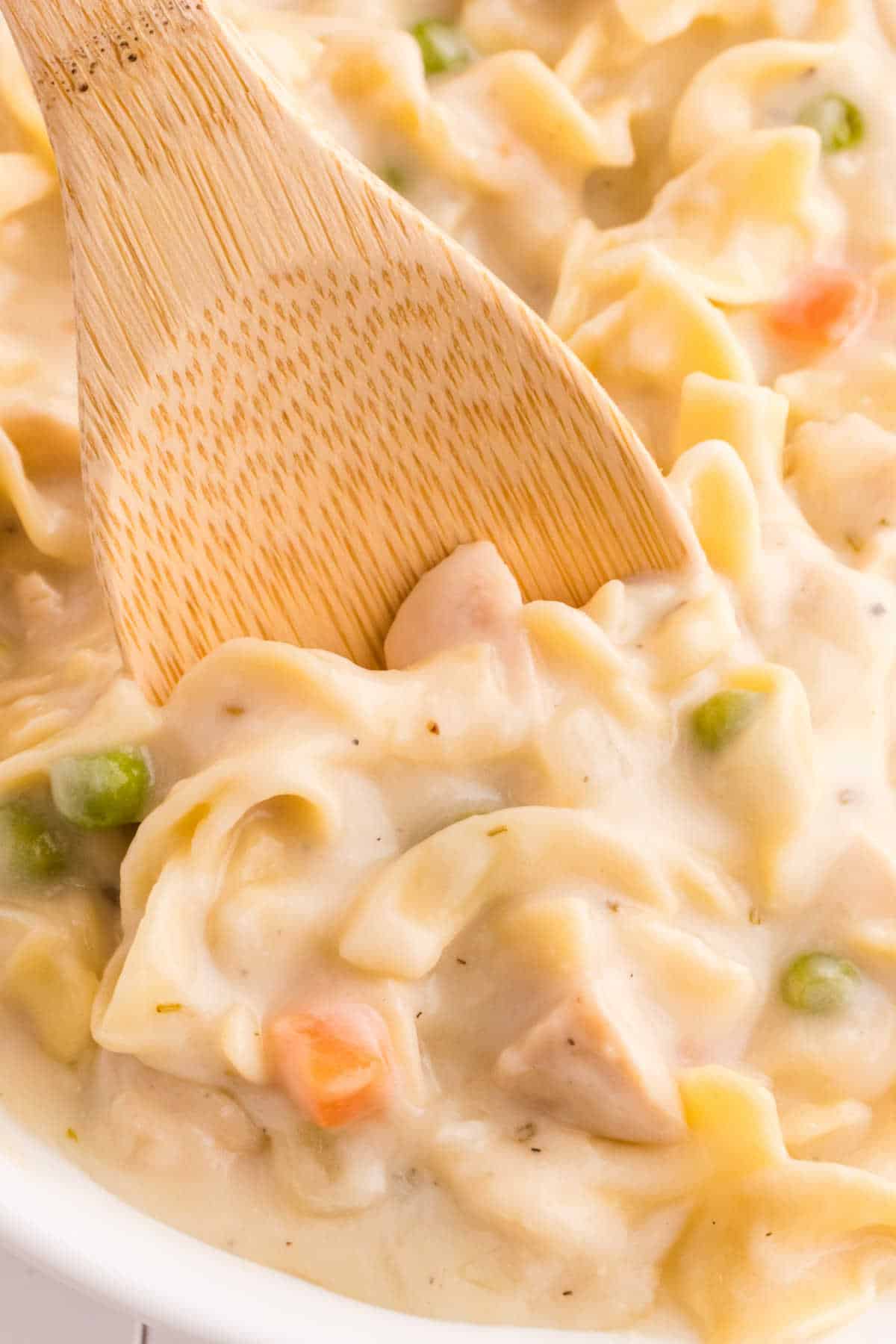 A pot of creamy chicken noodle soup with a wooden spoon in it.