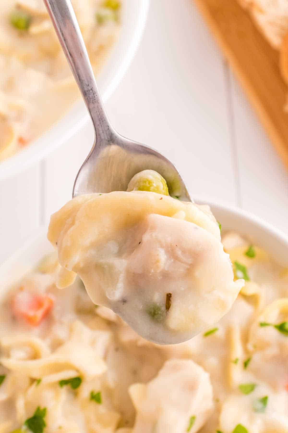 A spoon with creamy chicken noodle soup on it.