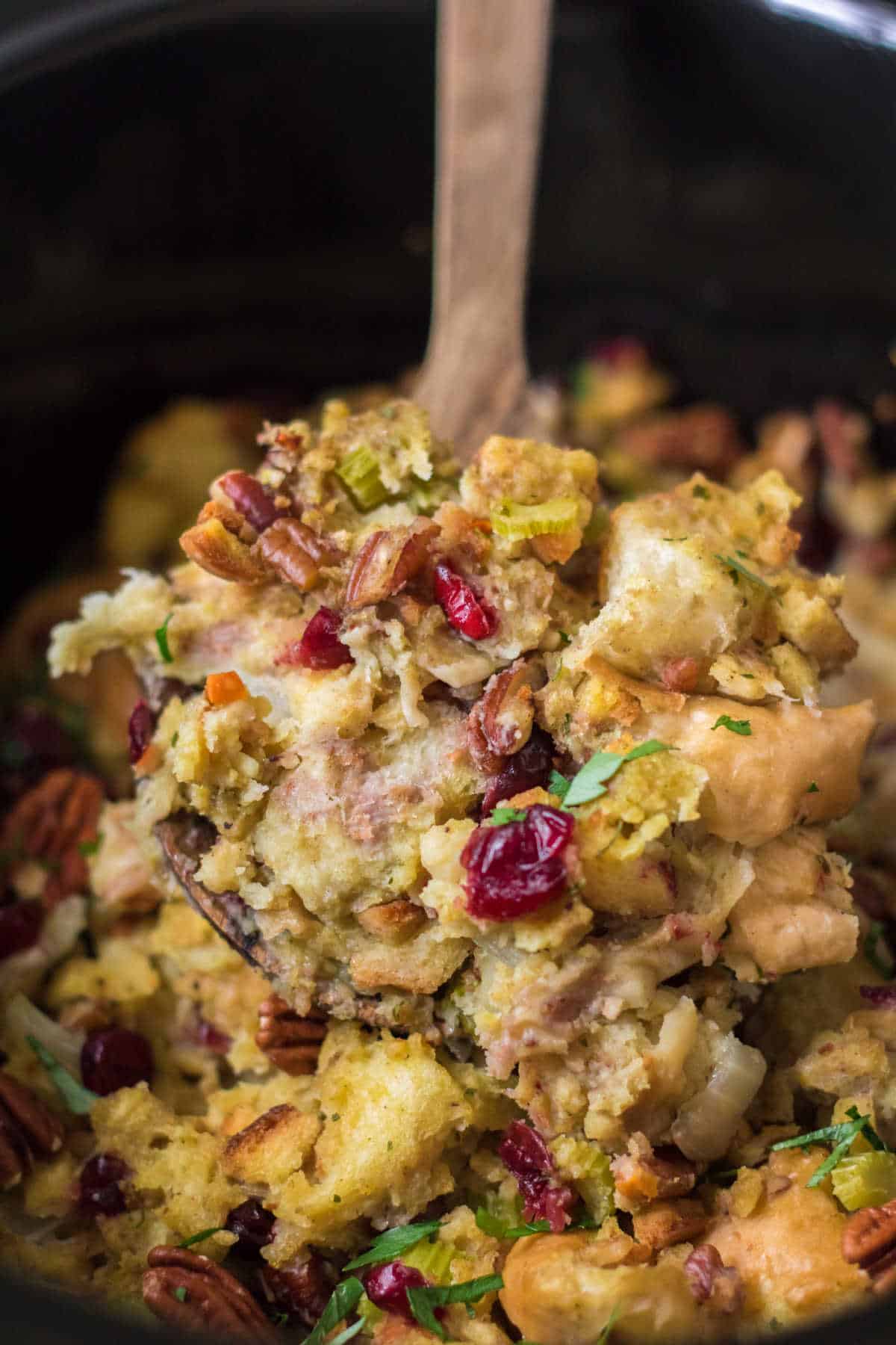 Cranberry pecan stuffing in a black crockpot with a wooden serving spoon.