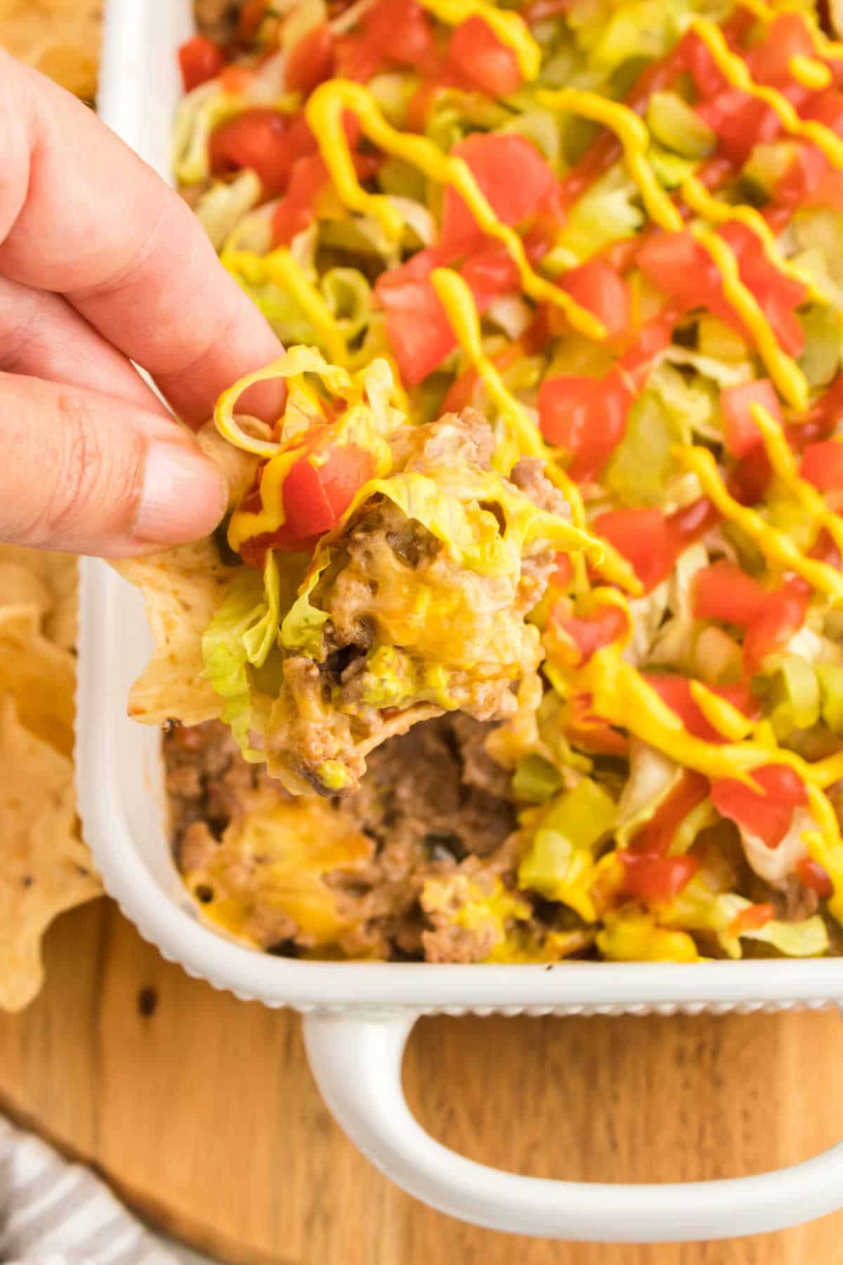 A hand holding a tortilla chip with cheeseburger dip.