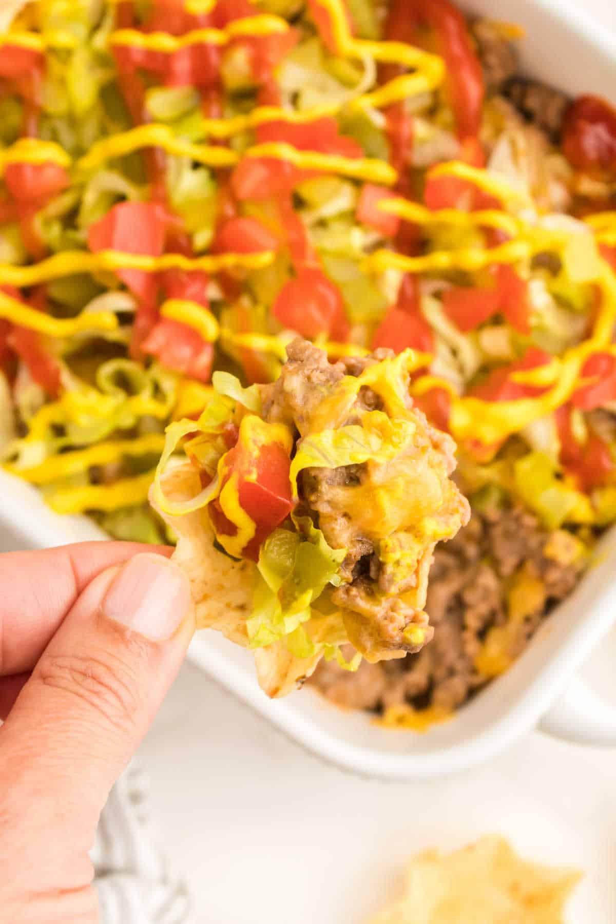 A hand holding a tortilla chip with cheeseburger dip.