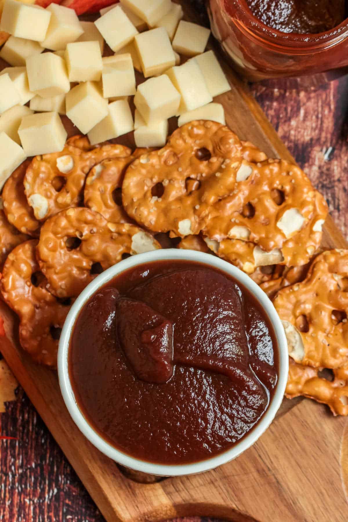 A bowl of apple butter surrounded by pretzels and cheese cubes.