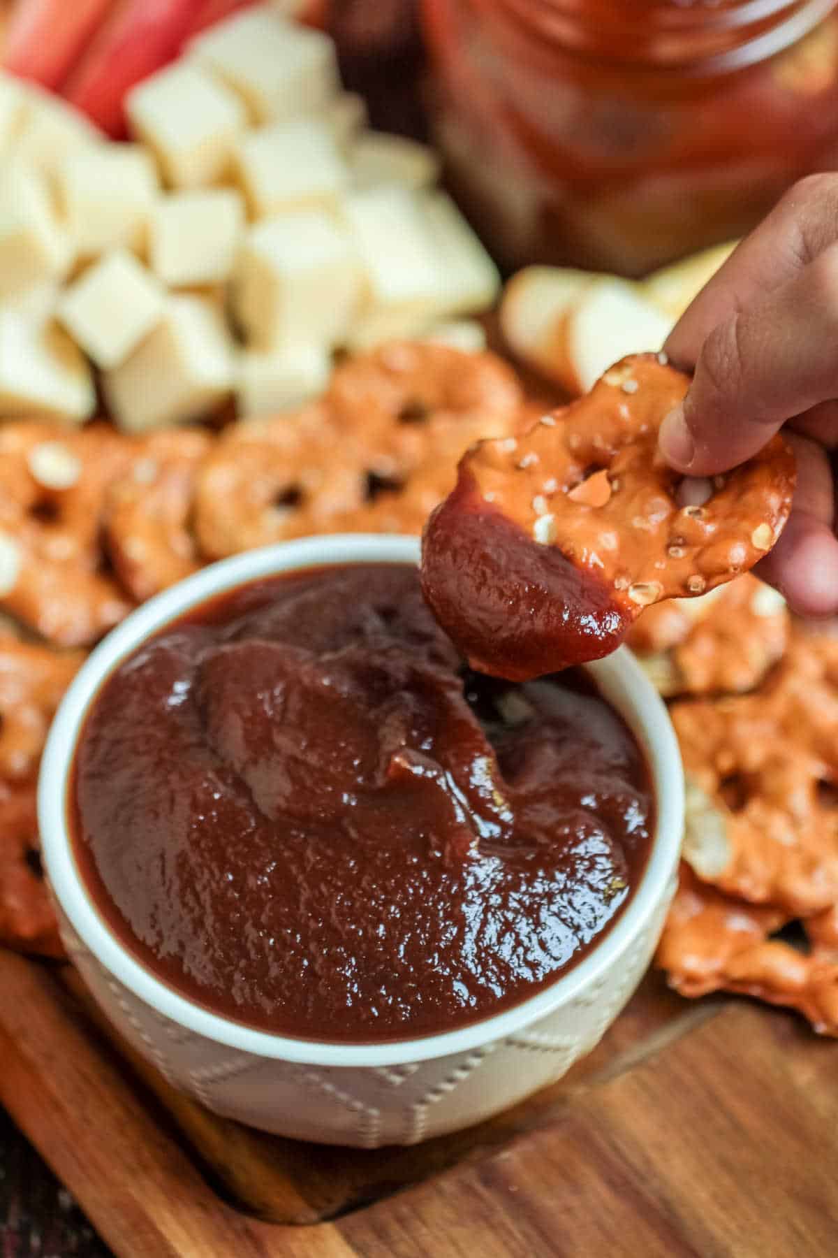 A hand dipping a pretzel in a bowl of apple butter.