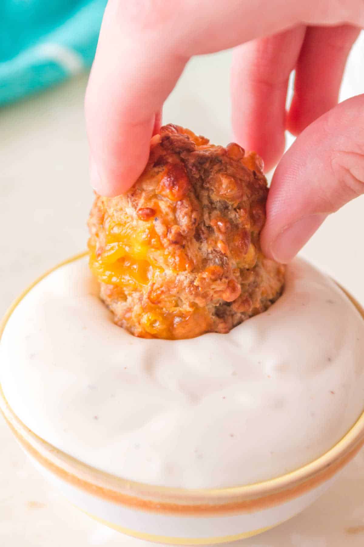 A hand dipping a sausage ball in ranch dip.