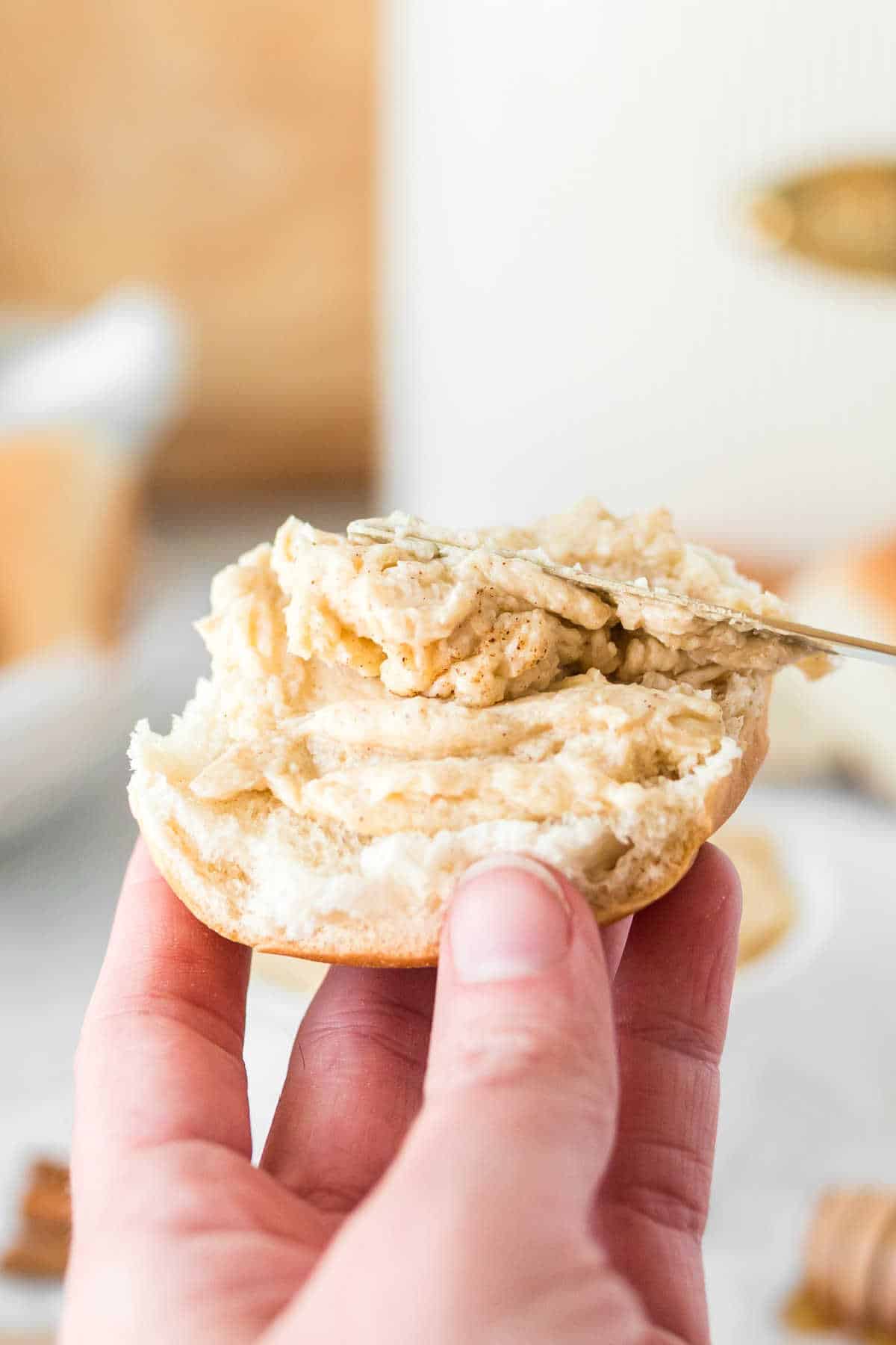 A butter knife spreading cinnamon butter on a dinner roll.