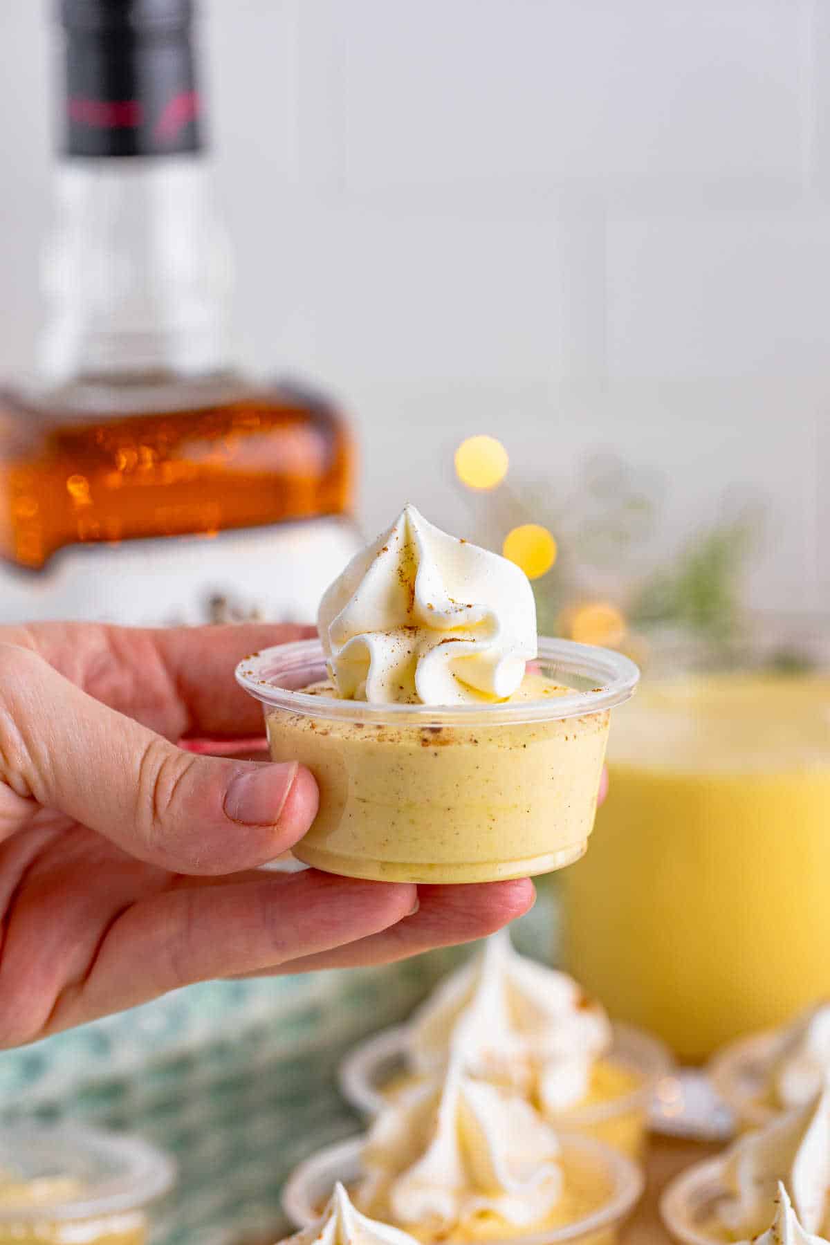 A hand holding an eggnog pudding shot.