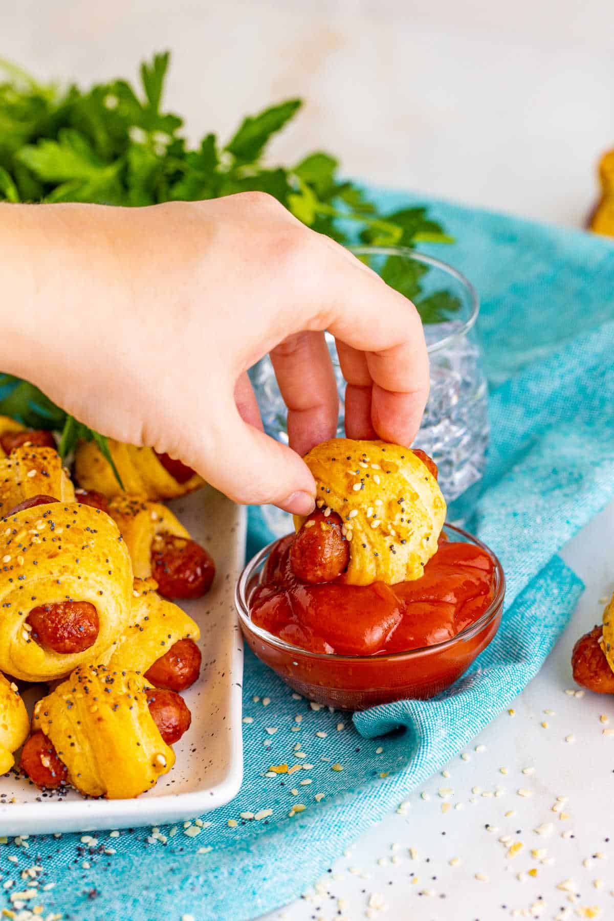 A hand dipping a pig in a blanket into ketchup.