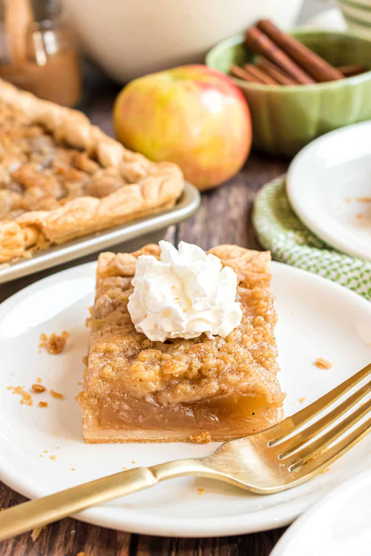 A slice of apple slab pie topped with whipped cream on a plate with a fork.