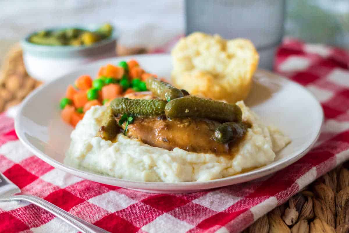 Pickle chicken served on plate with mashed potatoes, veggies and a bun.