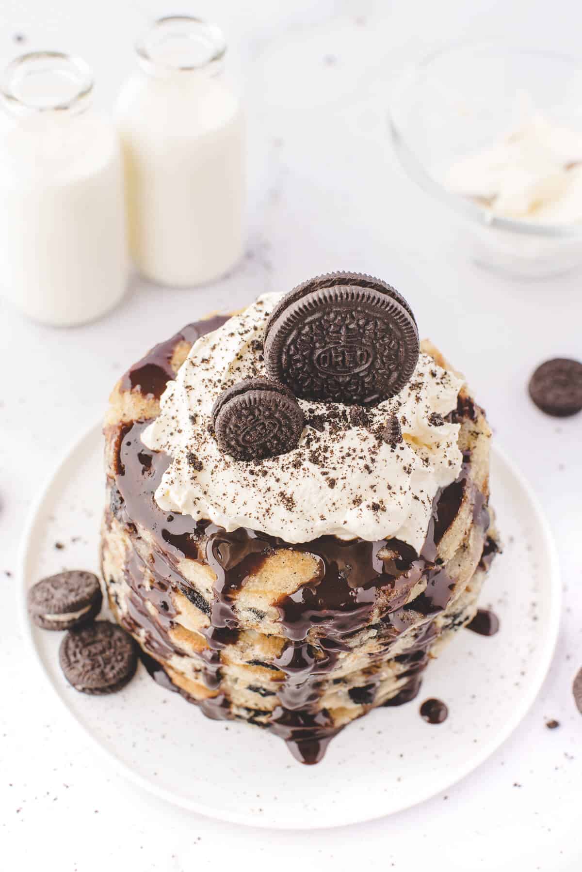 A stack of Oreo pancakes topped with whipped cream, chocolate sauce and Oreo cookies.