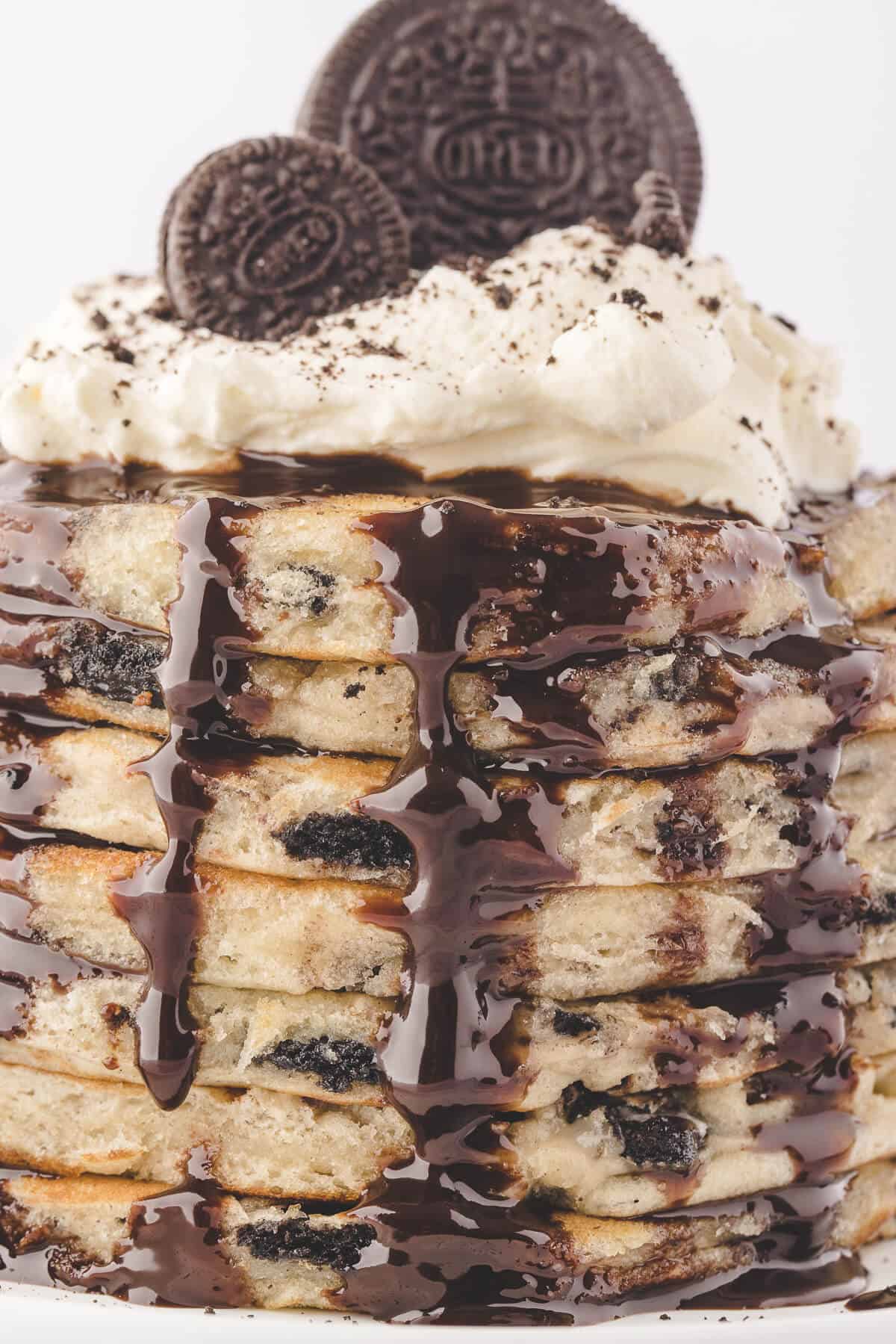 A stack of Oreo pancakes topped with whipped cream, chocolate syrup and Oreos.