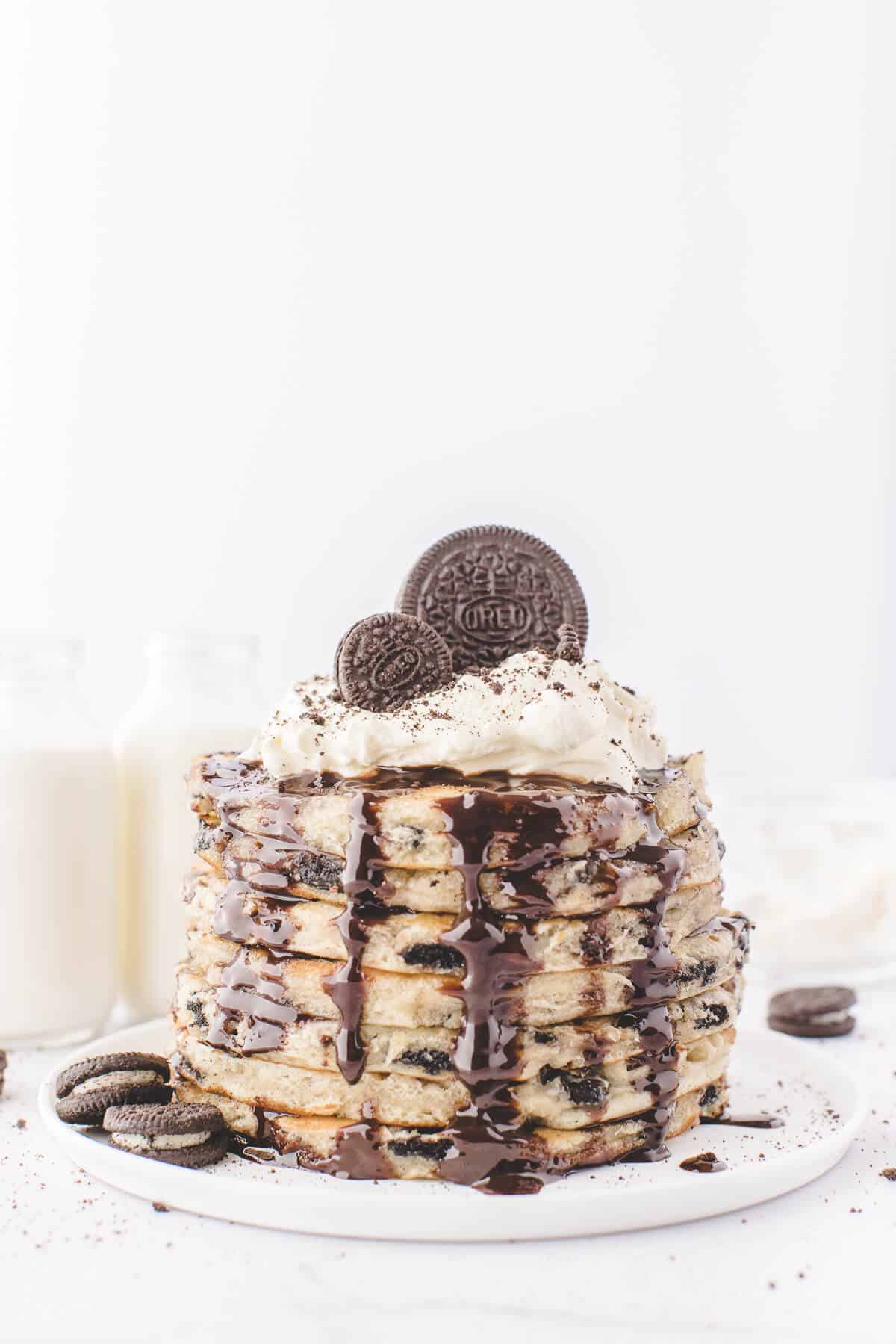A stack of Oreo pancakes topped with whipped cream, chocolate sauce and Oreo cookies.