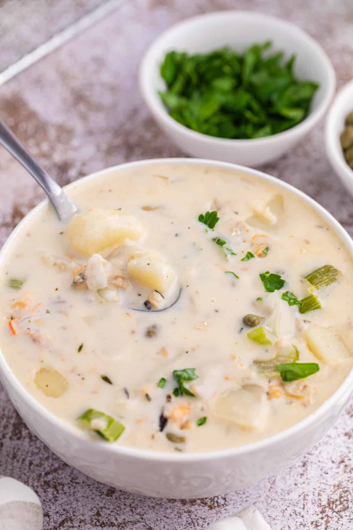 A white bowl of seafood chowder with a spoon.