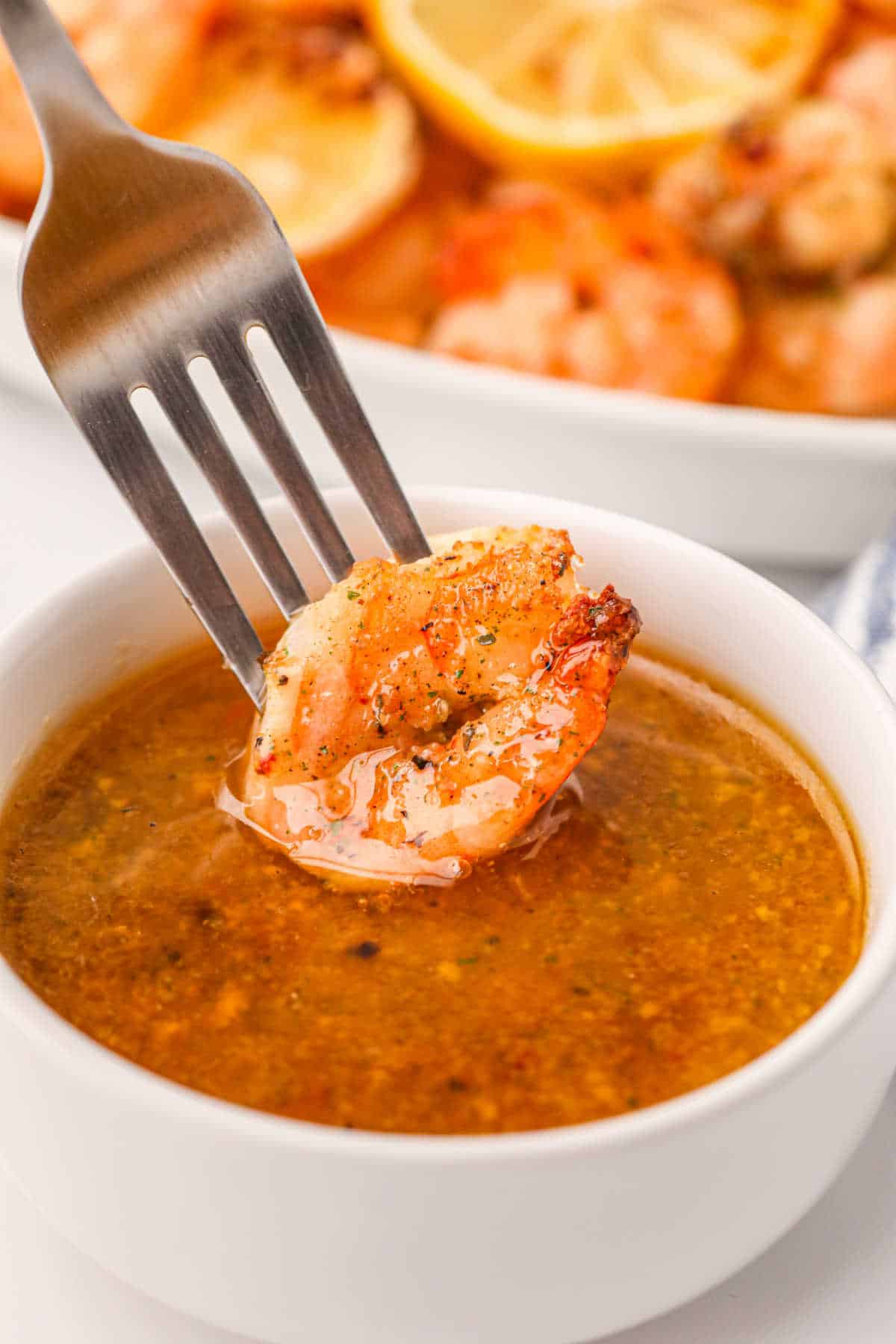 A fork with a shrimp on it dipping in a small bowl of sauce.