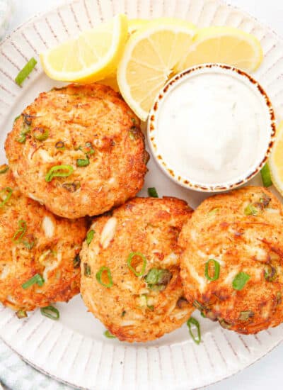 Air fryer crab cakes on a plate with tartar sauce and lemon.