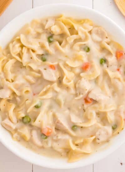 A white bowl of creamy chicken noodle soup.