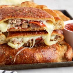 Meat calzones cut in half on a baking sheet with marinara sauce.