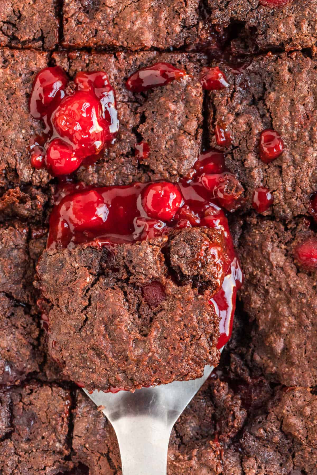 A spatula with a slice of black forest dump cake over a pan.