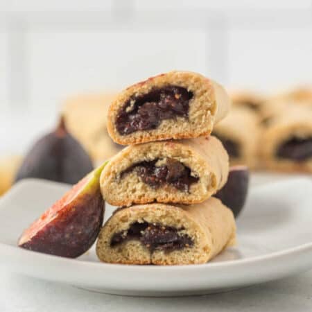A stack of three fig newtons on a plate with a sliced fig.
