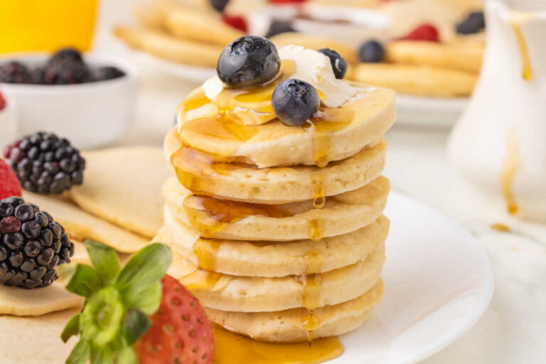 A stack of mini pancakes topped with butter, blueberries and maple syrup.