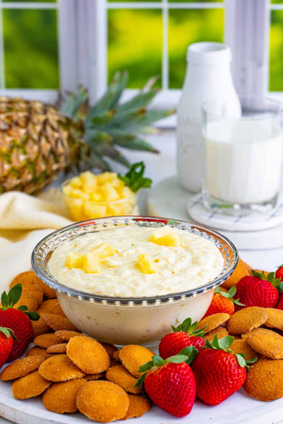 Pineapple dip in a bowl surrounded by cookies and strawberries.