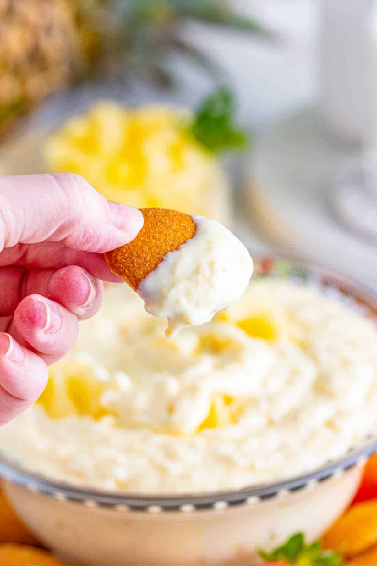 A hand holding a cookie with pineapple dip.