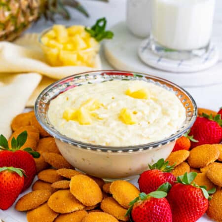 Pineapple dip in a bowl surrounded by cookies and strawberries.