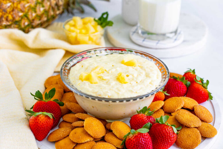 Pineapple dip in a bowl surrounded by cookies and strawberries.