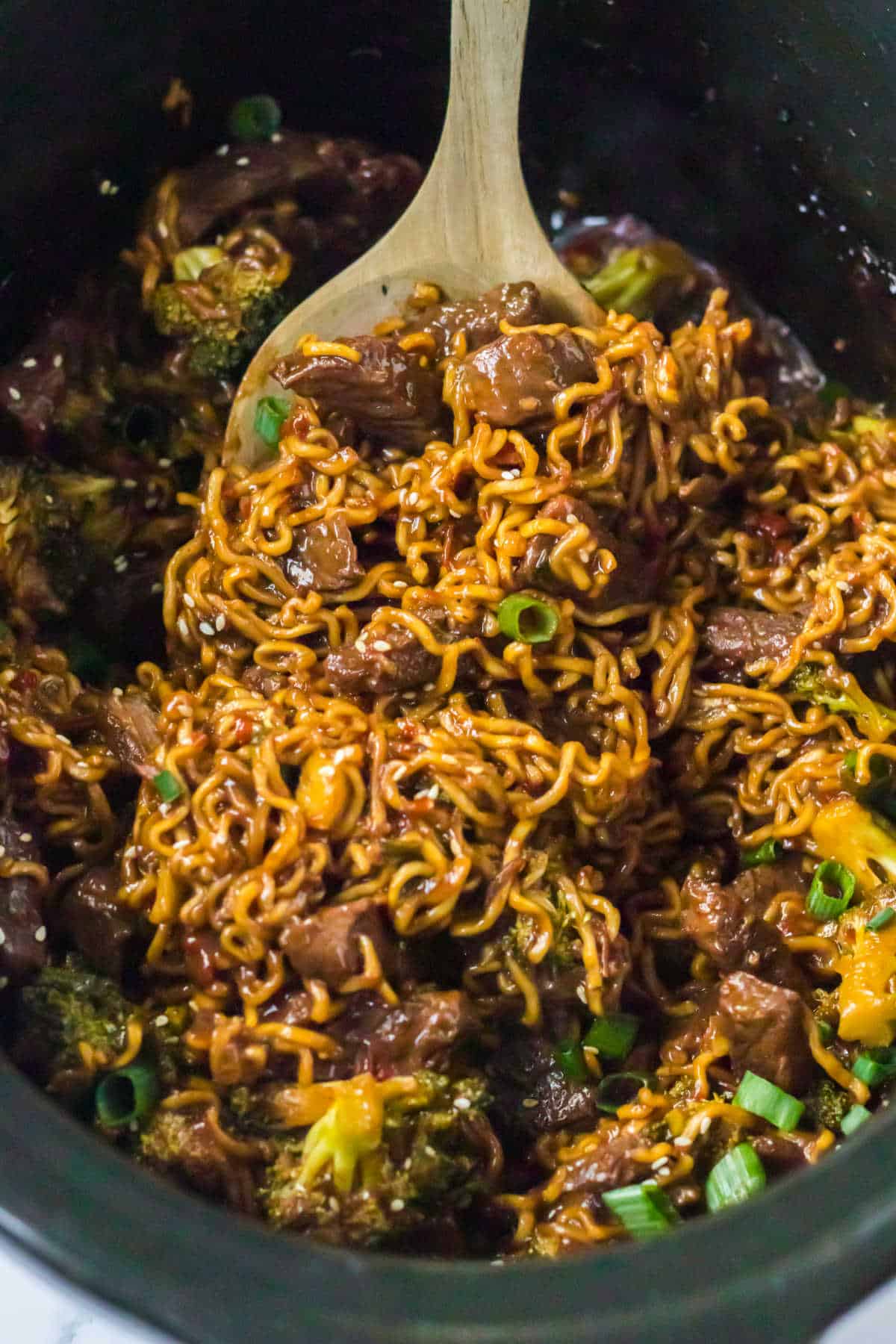 Beef and broccoli ramen with a wooden spoon in a crockpot.