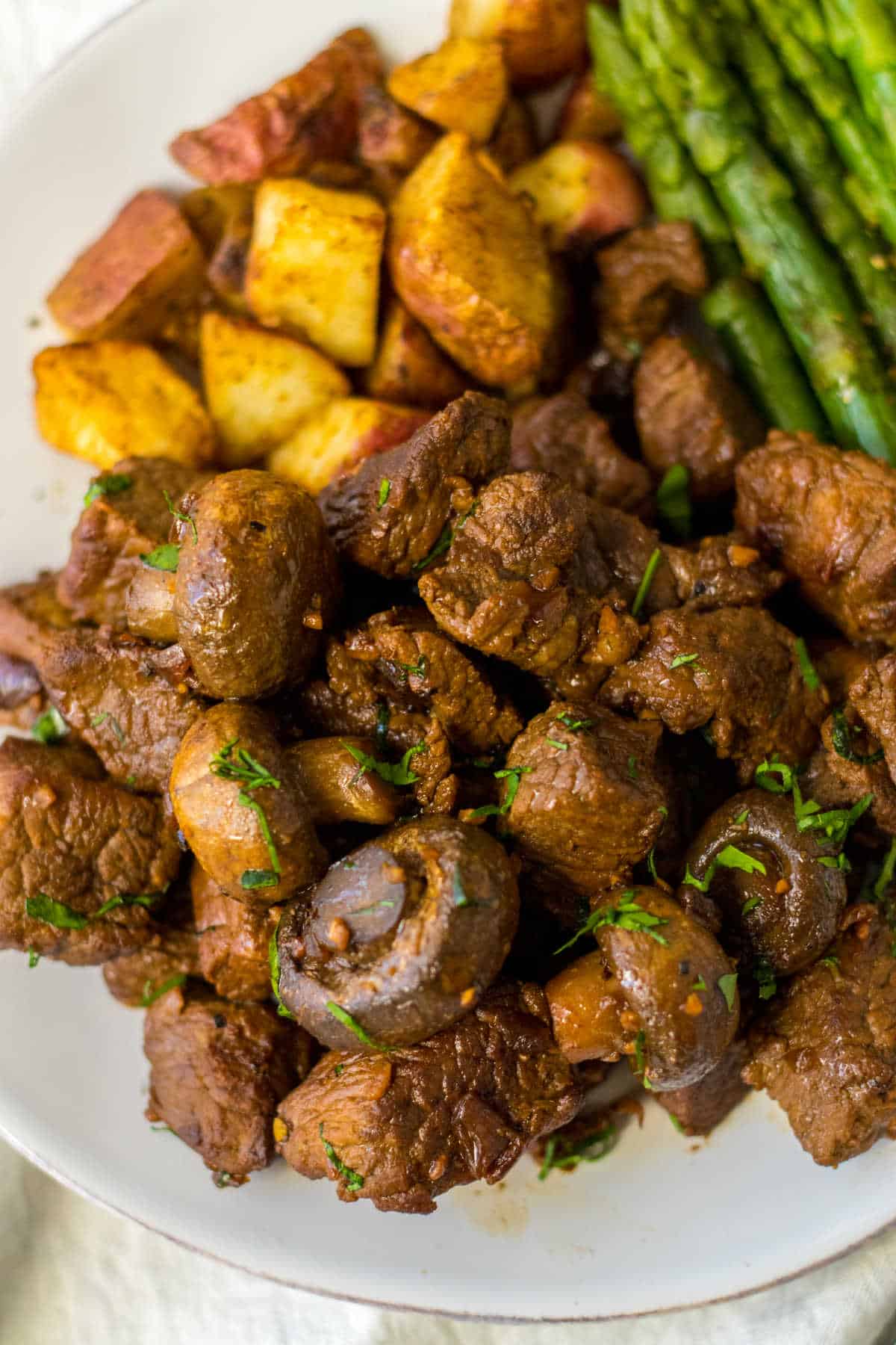 Slow cooker mushroom steak bites on a plate with roasted potatoes and asparagus.